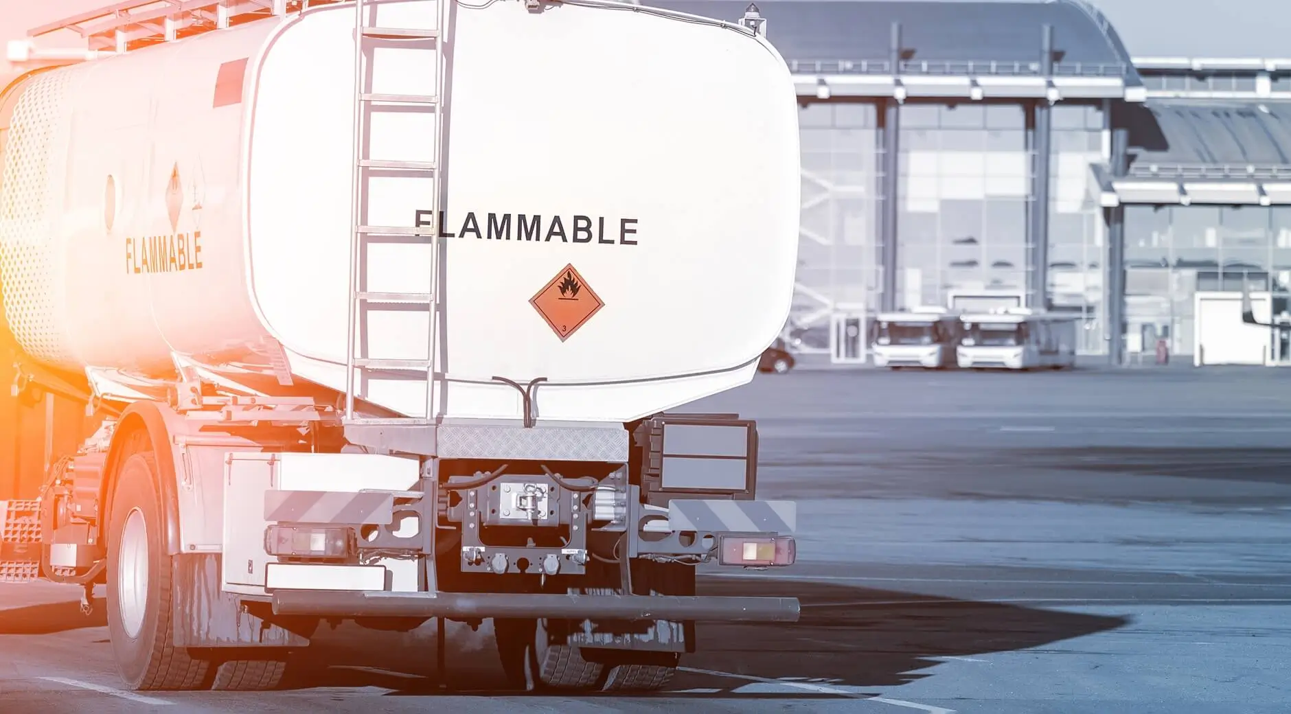 Fuel tanker truck with flammable material warning sign parked near an airport terminal.